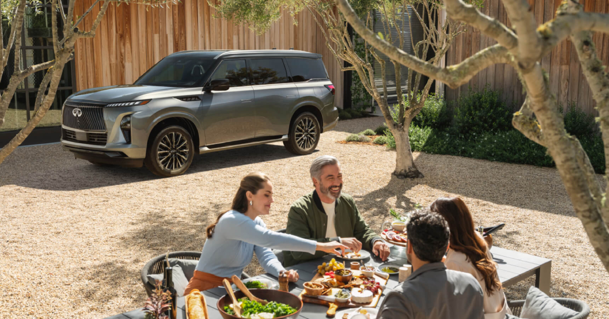 a 2025 INFINITI QX80 parked in a backyard while a family is having a picnic at the table