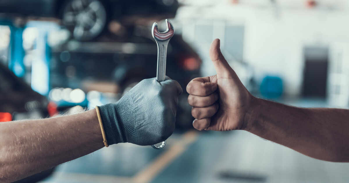 a gloved hand holding up a wrench and another hand in a thumbs up