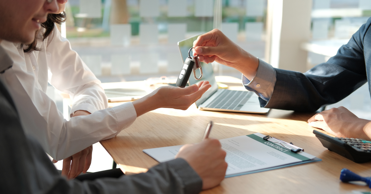 a man signing a contract and a salesman handing the woman the car keys