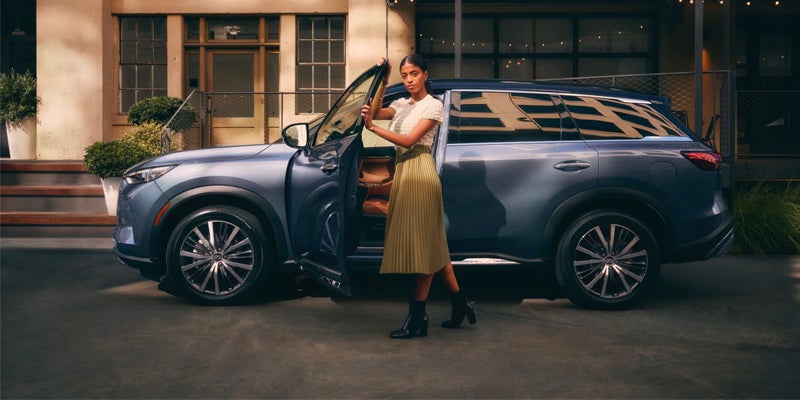 A person stands next to an open door of a blue Car parked in an outdoor courtyard area