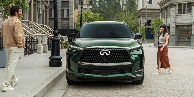 A green Infiniti SUV parked on a city street between two people