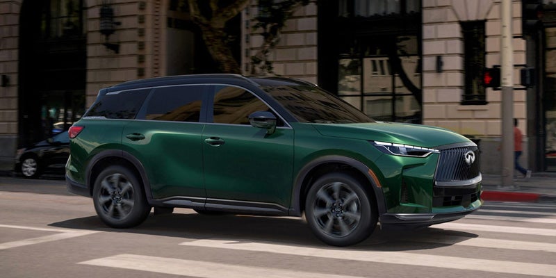 Side profile of a green Infiniti SUV driving through a city intersection