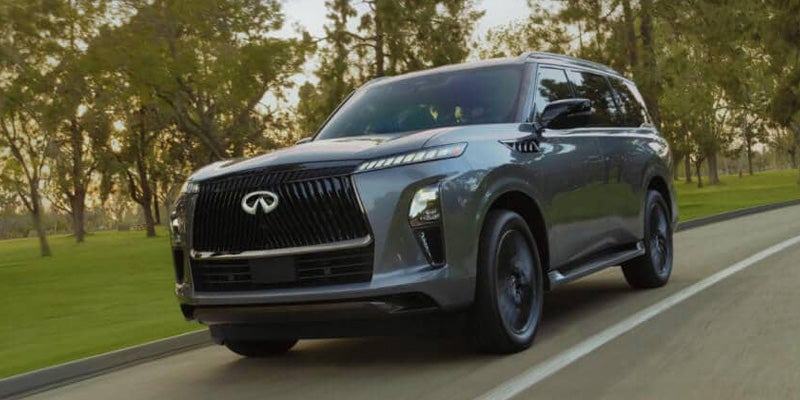 A grey Infiniti QX80 SUV driving on a road lined with trees